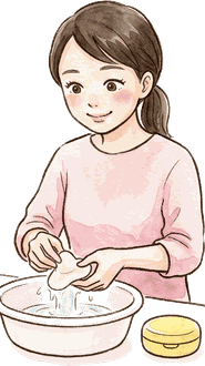洗面ボウルの前で乳頭保護器を両手で洗っているママ。横に黄色い丸いケース
