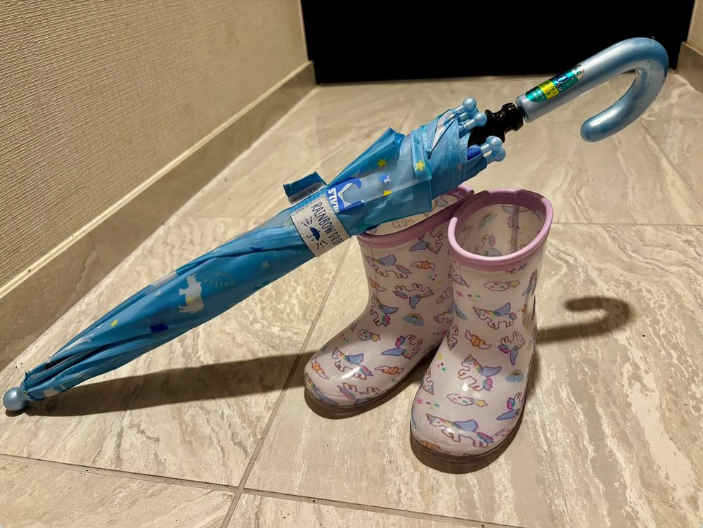 玄関の床に置いた、ユニコーン柄の子ども用長靴と水色の子ども用傘