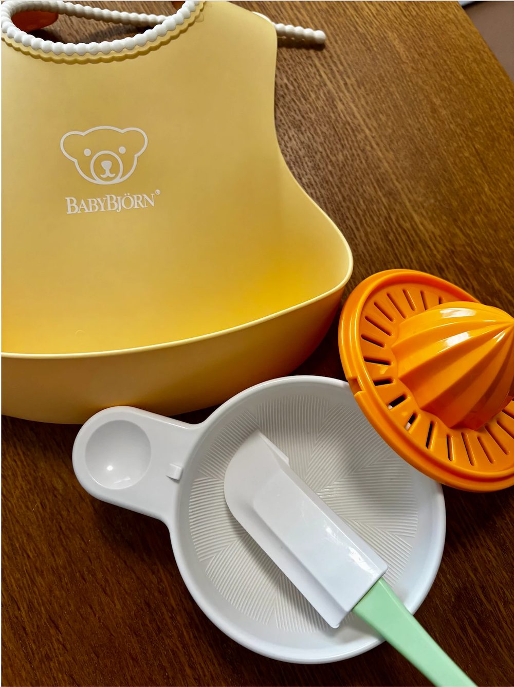 黄色いシリコンのスタイ、白いすりつぶし用の器とへら、オレンジ色の果汁しぼり